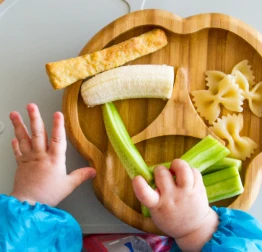 A babies hands grabbing food from a bowl